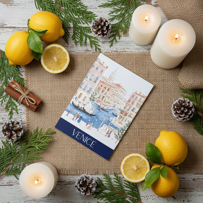 Christmas greeting card with Venice illustration surrounded by lemons, candles, and pine cones on a wooden surface.