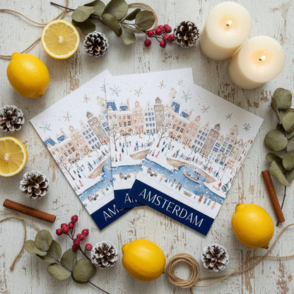 Christmas cards with Amsterdam design surrounded by lemons, candles, and decorative elements on a wooden surface.