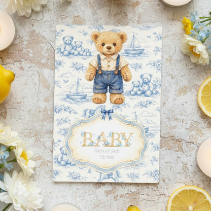 Personalised baby card with teddy bear design on a textured surface with flowers and lemons.