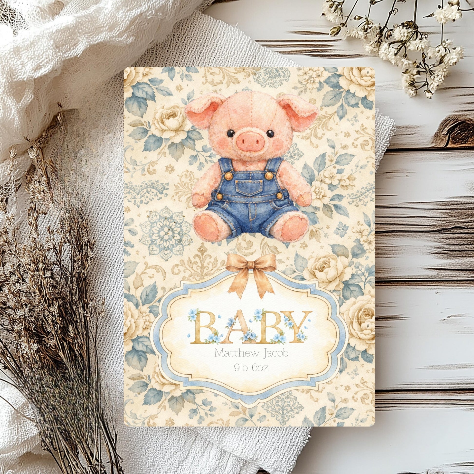 Baby card with a pig illustration and floral design on a wooden surface.