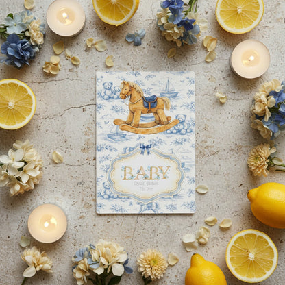 Rocking horse baby card with rocking horse design surrounded by lemons and flowers on a textured surface