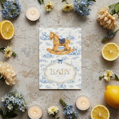 Baby card with rocking horse design surrounded by lemons and flowers on a textured surface